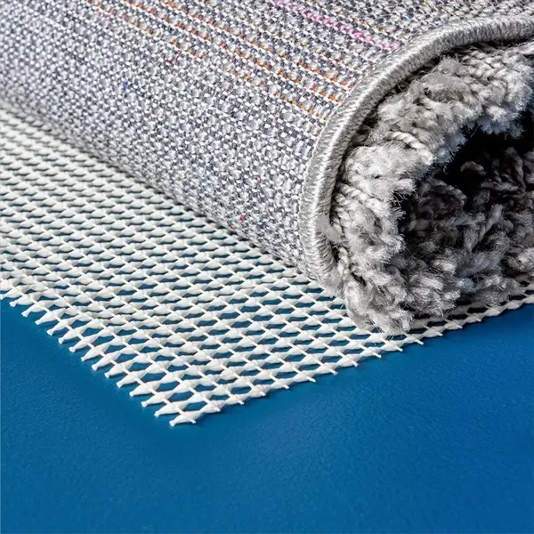 White open-mesh rug gripper beneath a rolled carpet on a blue floor.